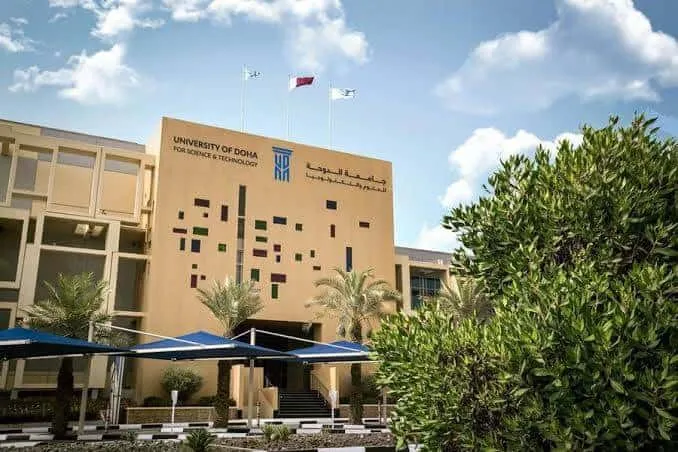 University of Doha building with trees and flags.