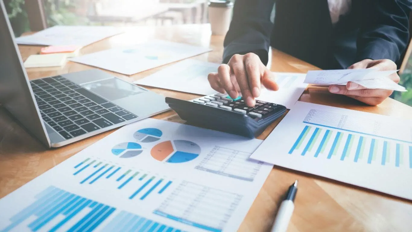 Person calculating finances with laptop and charts.