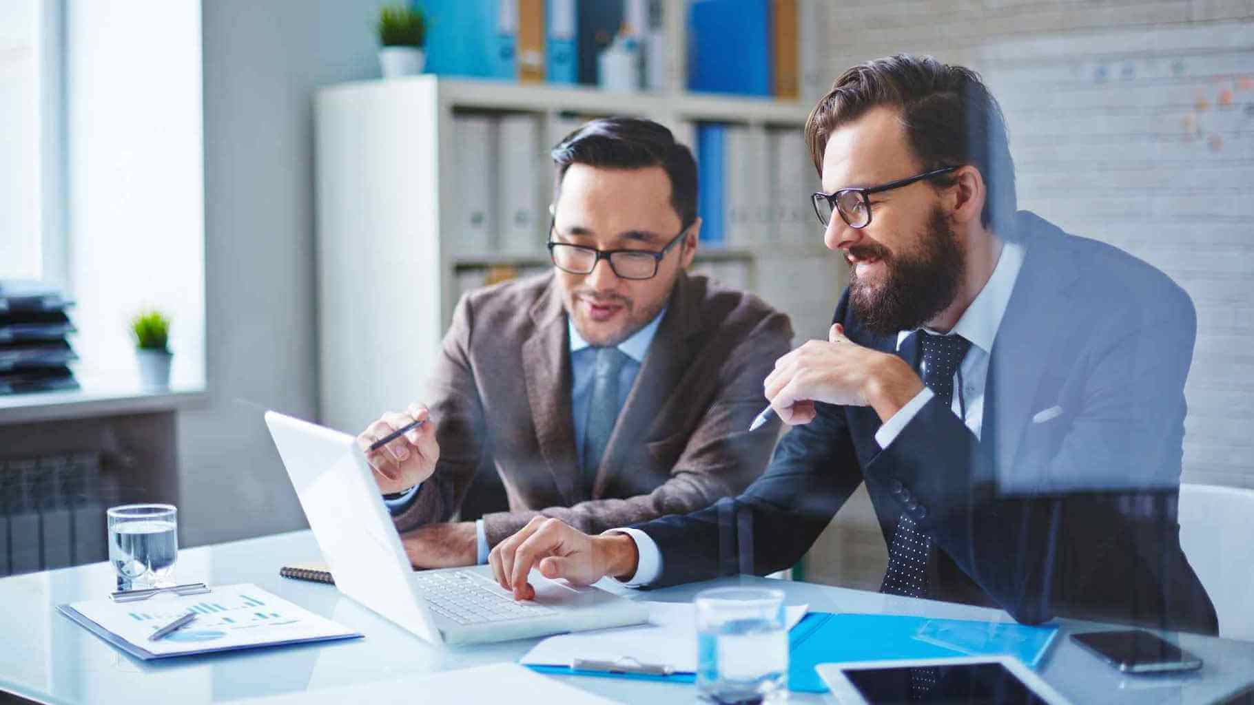 Two businessmen discussing at laptop in office.