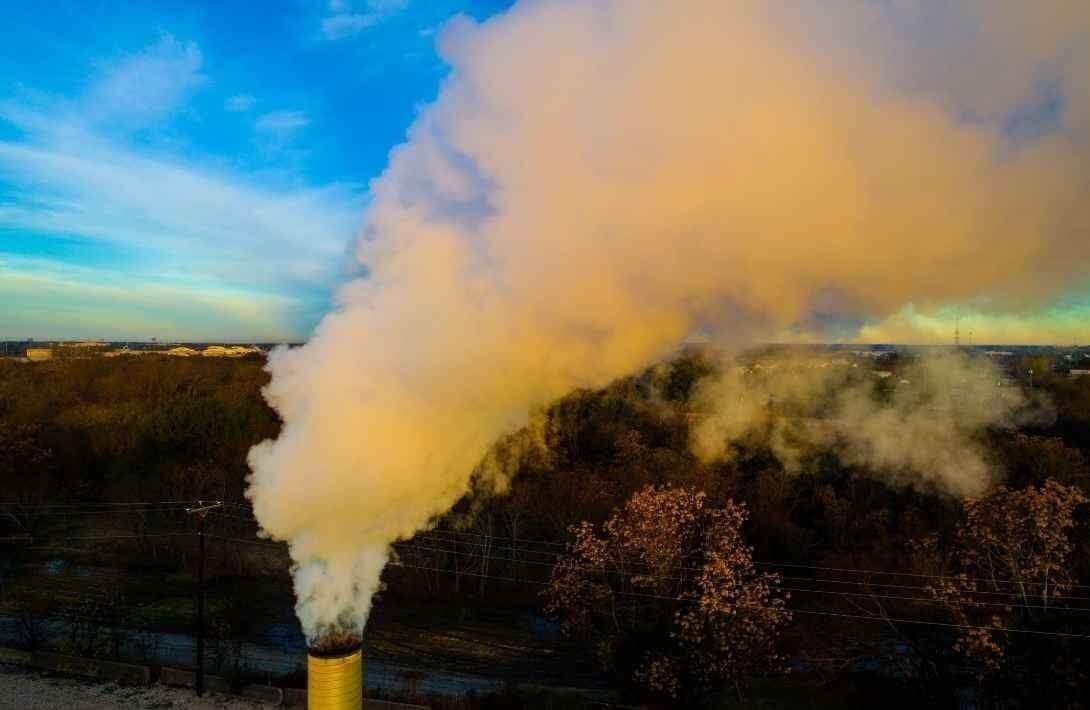 Smoke rising from industrial chimney against blue sky.