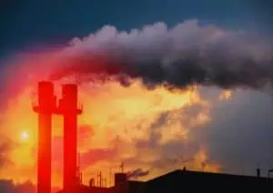 Factory smokestacks emitting smoke against fiery sunset sky.