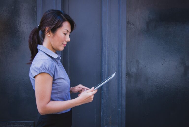 Woman reading a tablet outside on a sidewalk.